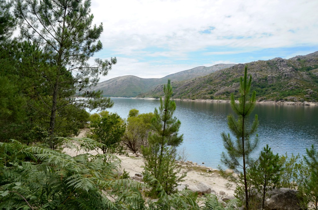 Ein See mit Felsen und Bäumen am Ufer unter blauem Himmel.