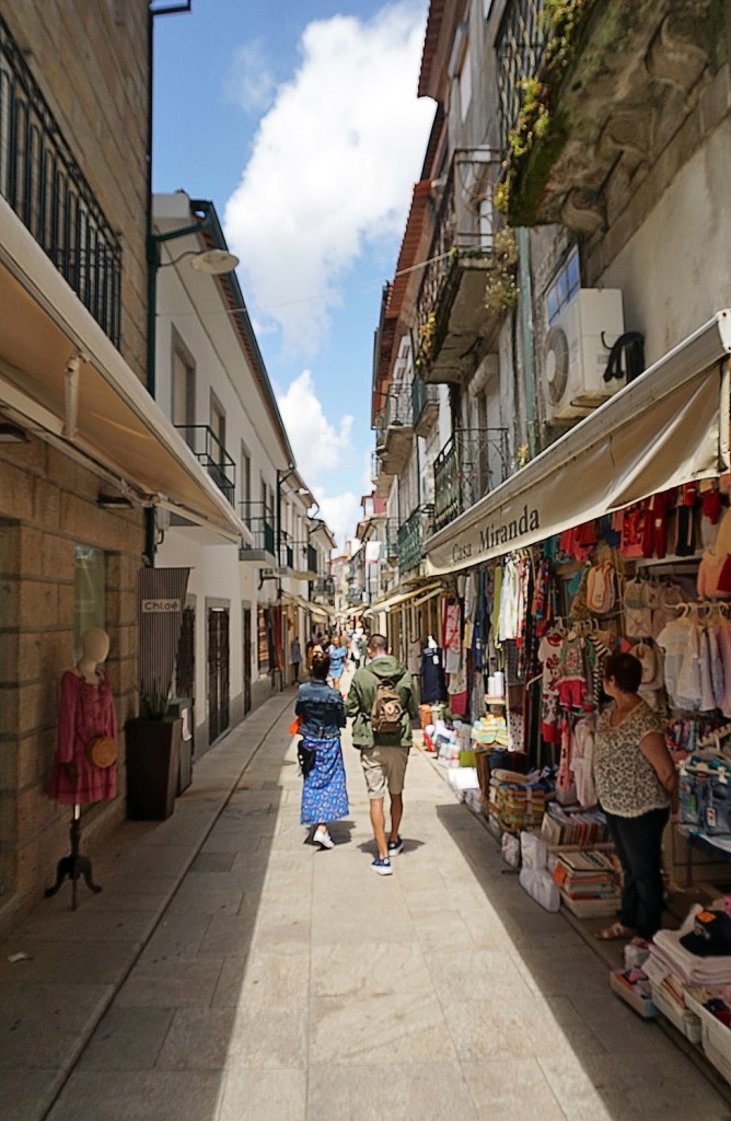 Eine belebte Gasse mit Geschäften und Menschen führt durch eine Stadt.