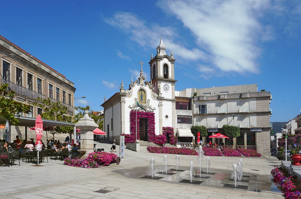 Eine Kirche mit Brunnen und Cafés auf einem belebten Platz.