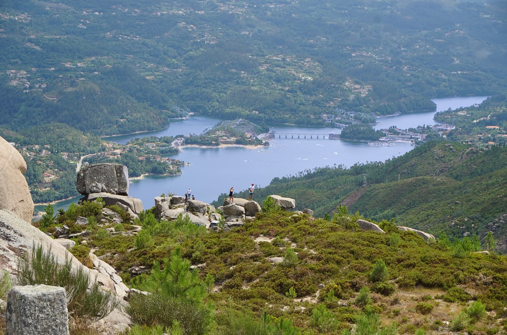 Aussicht auf einen See und eine Staumauer von einem felsigen Bergkamm