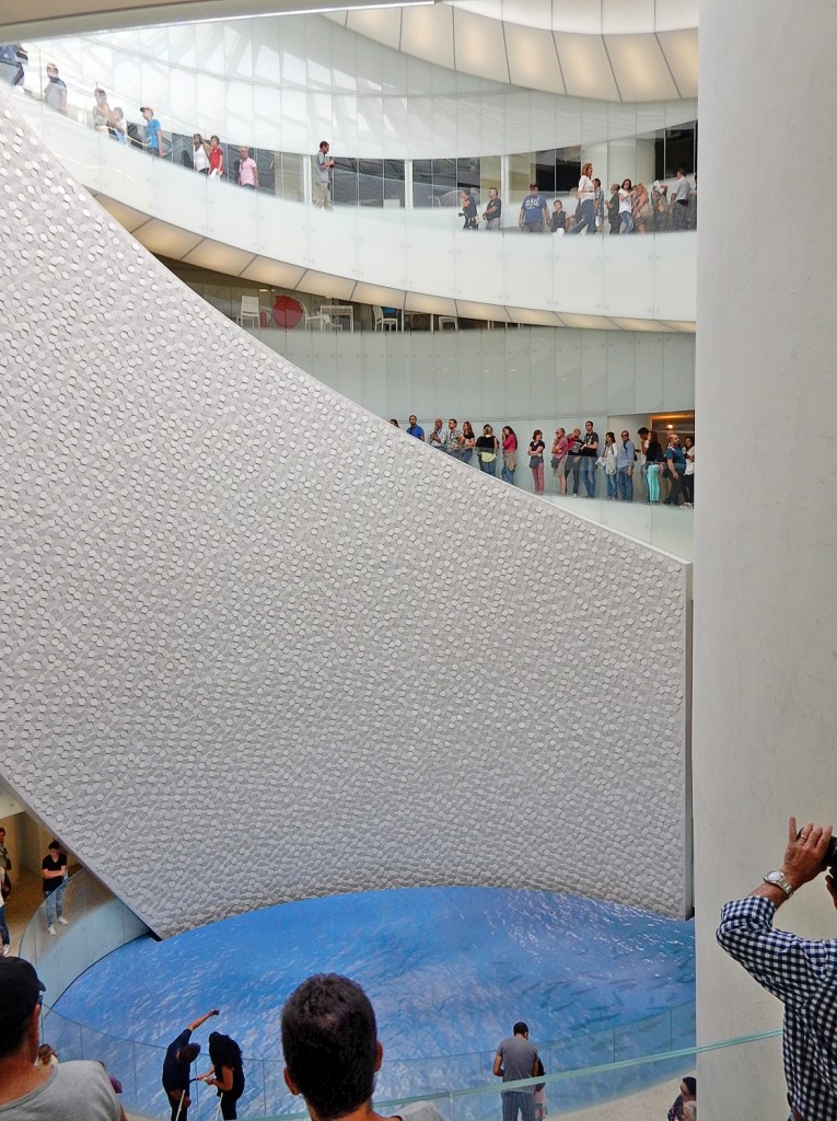 Besucher betrachten eine architektonische Installation mit blauen Wasseroberfläche im Innenraum.
