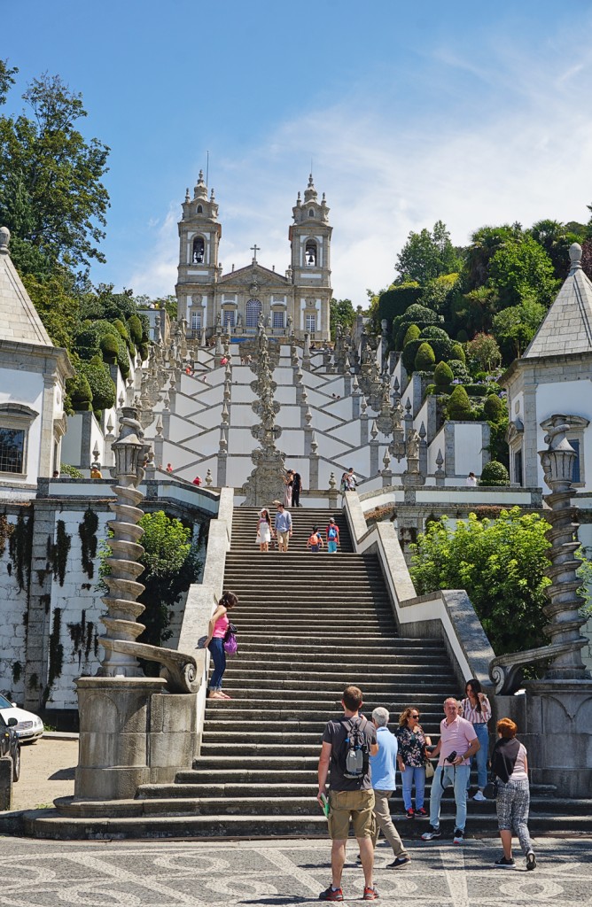 Steps lead up to a church with ornate fountains and gardens in a sunny landscape