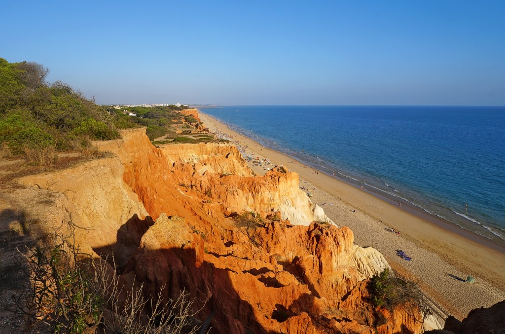 Red cliffs overlook a sandy beach and turquoise ocean under a clear sky