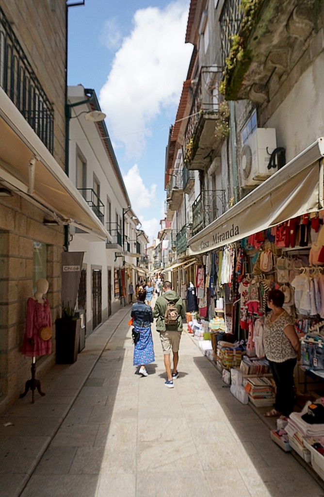 People stroll down a narrow street lined with shops and balconies