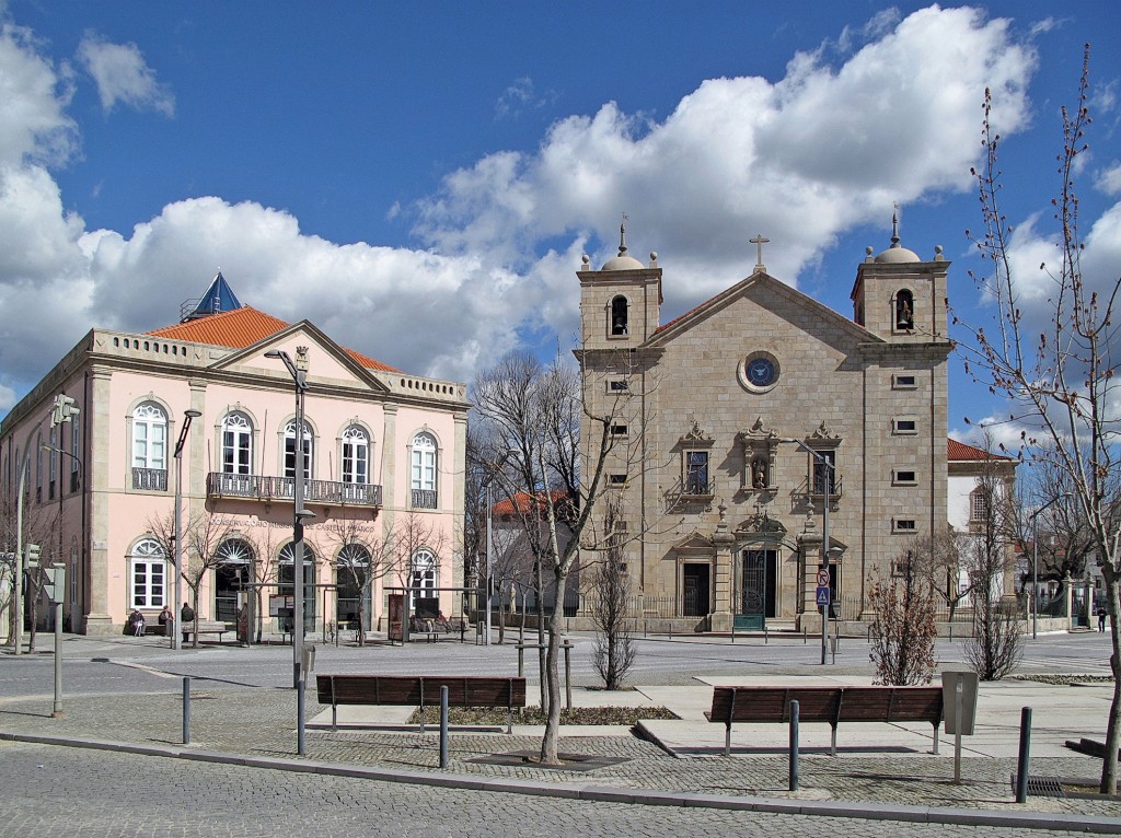Historische Gebäude mit Fassaden und Türmen dominieren einen sonnigen Platz.