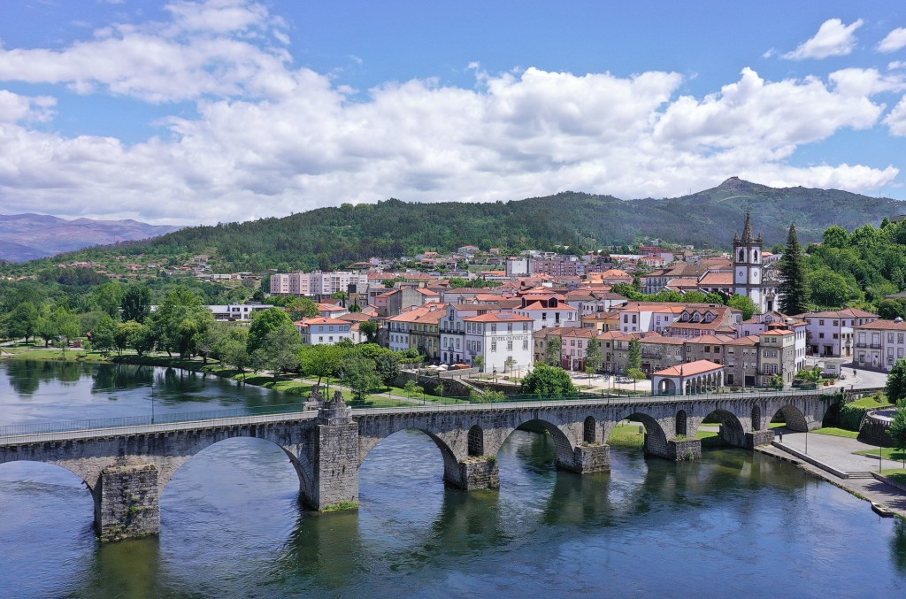 Historic town with red roofs sits beside a river spanned by an arched stone bridge