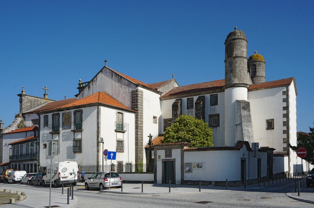 Ornate white building with red tiled roof and tower stands on a street with parked cars