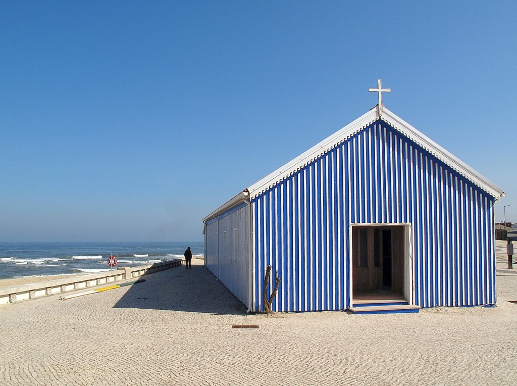 Eine blaue Strandkapelle steht vor dem Ozean und blauem Himmel.