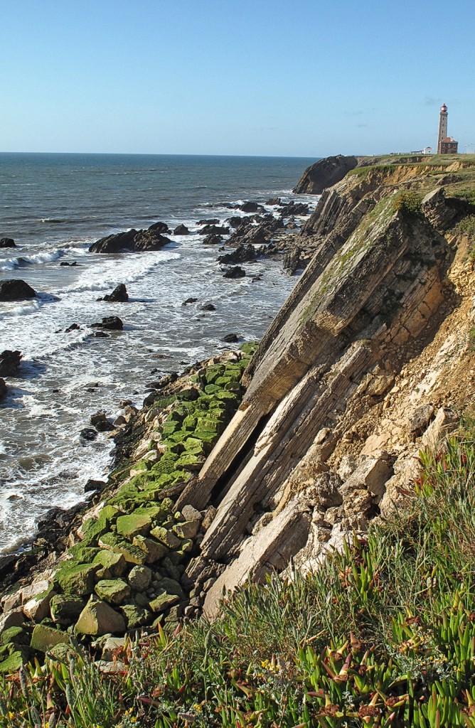 Steile Klippen treffen auf das Meer mit einem Leuchtturm in der Ferne