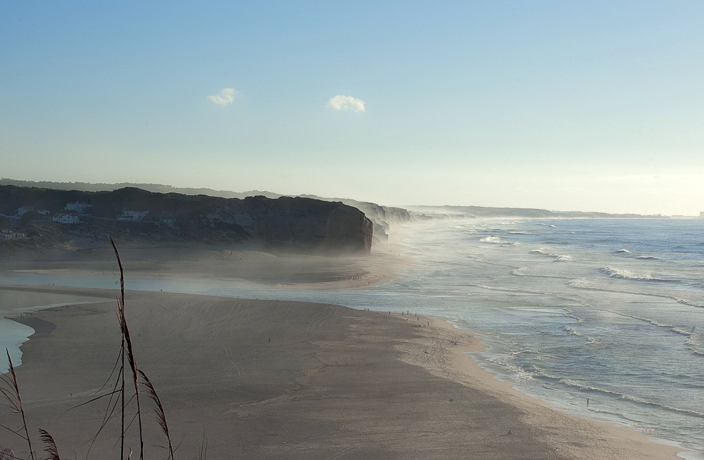 Weitläufiger Sandstrand mit Wellen und Nebel am Horizont