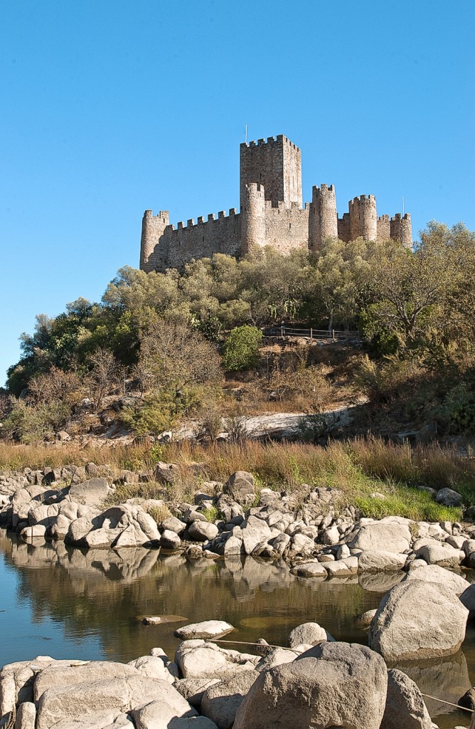 Eine Burg thront auf einem Hügel mit Blick auf einen Fluss im Sonnenlicht.