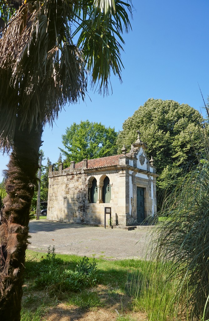 Ornate stone chapel stands amidst lush greenery on a sunny day.