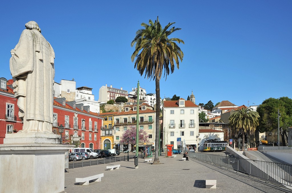 Ein Denkmal steht vor bunten Häusern und Palmen in einer Stadt.