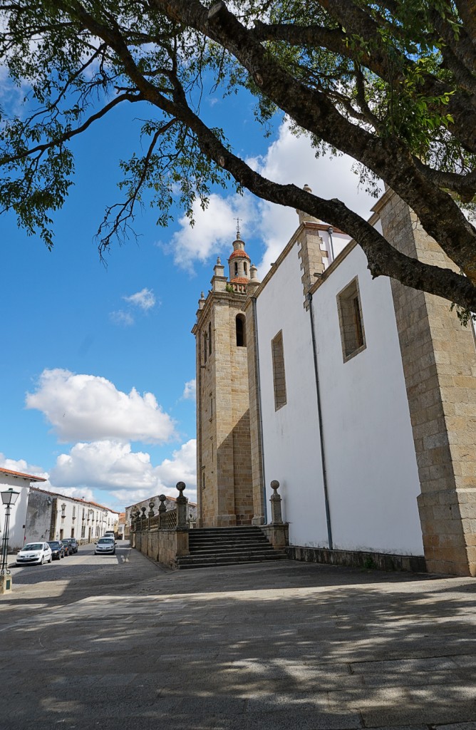 A grand stone church with a tall bell tower stands in a sunny town square.