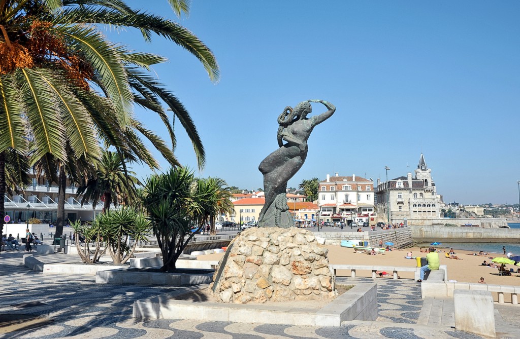 Eine Statue auf einem Sockel mit Strand und Gebäude im Hintergrund