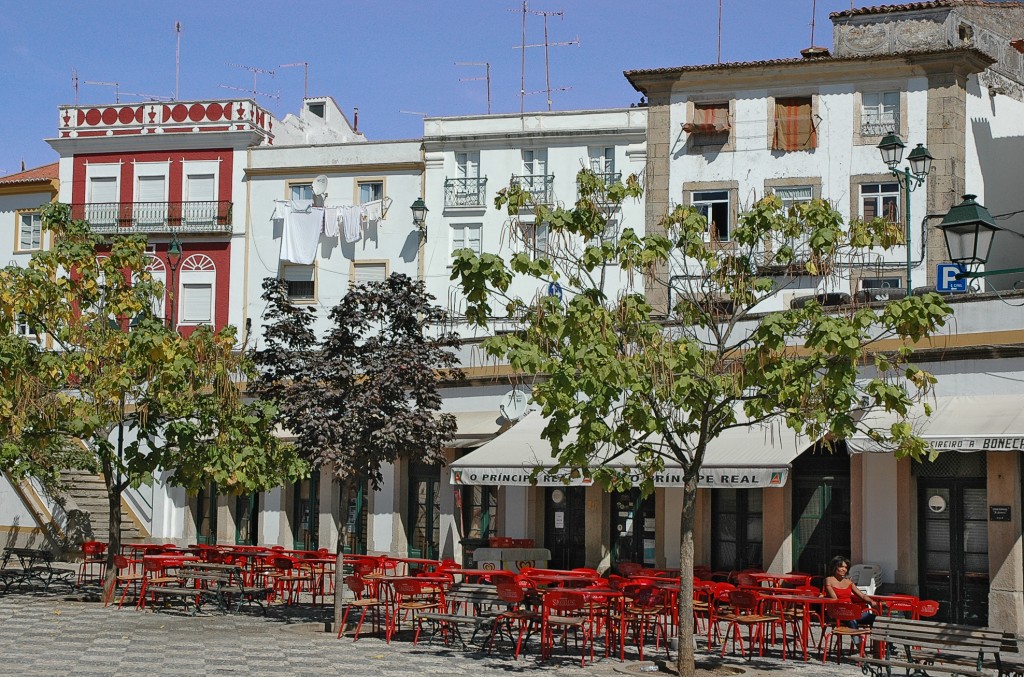 Ein Platz mit Cafés und roten Tischen unter Häusern mit traditioneller Architektur