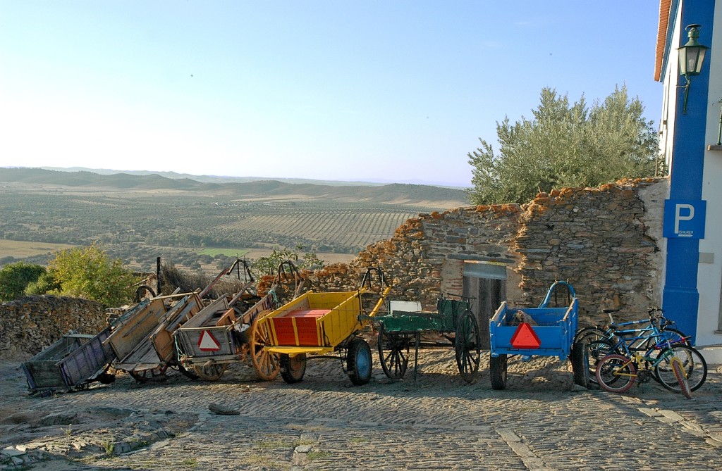 Alte Karren und Fahrräder stehen vor einer Steinmauer mit Blick auf eine Landschaft