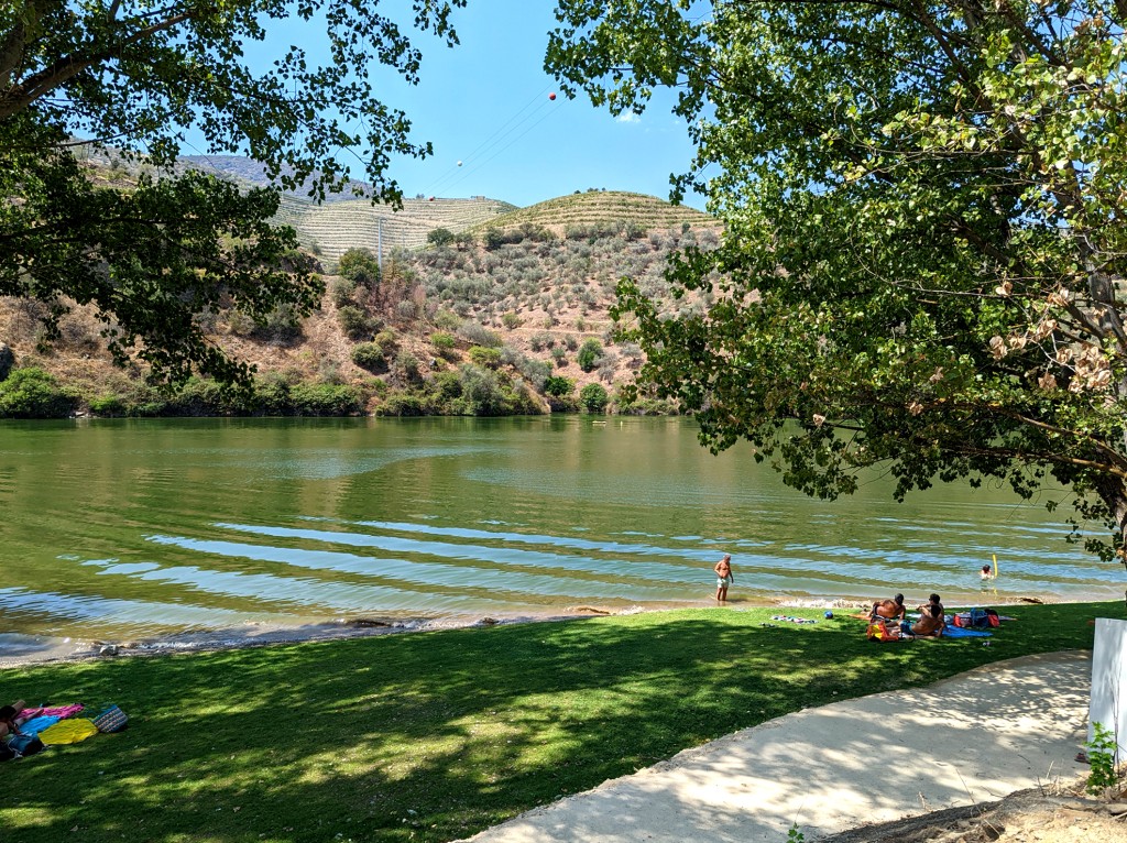 People relax by a lake with a grassy bank and hillside backdrop.