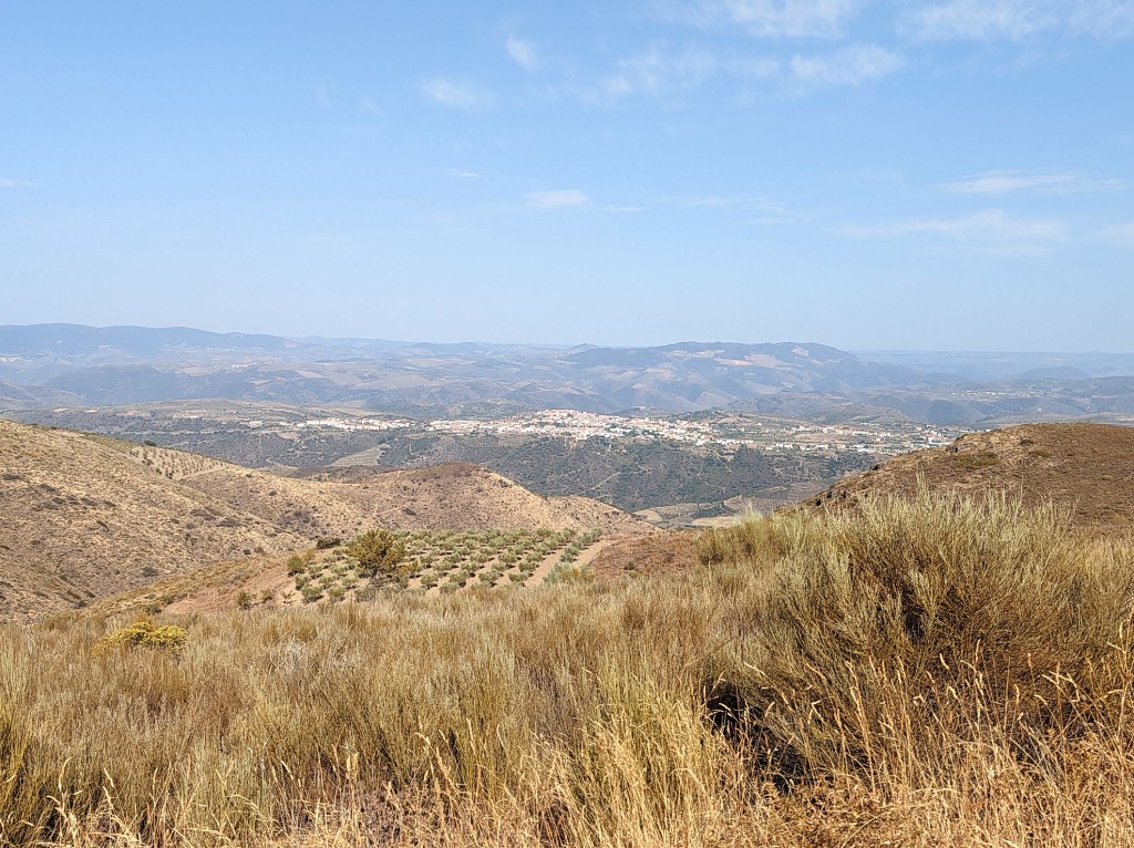 Grassy hillside overlooks a town nestled in a valley surrounded by mountains