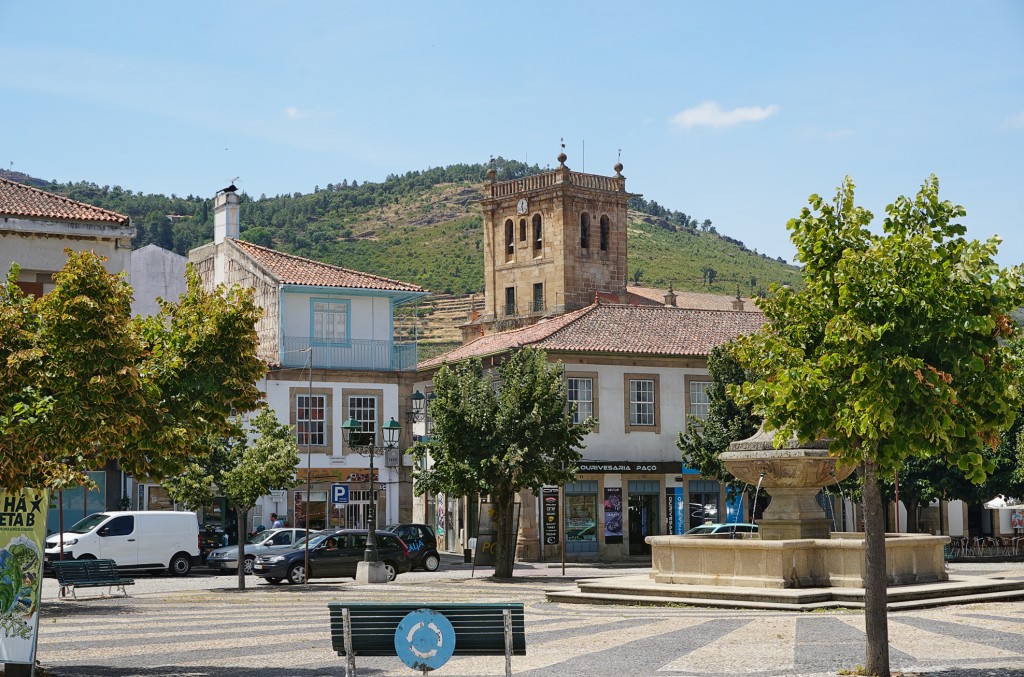 A town square features a historic building with an ornate tower and surrounding greenery