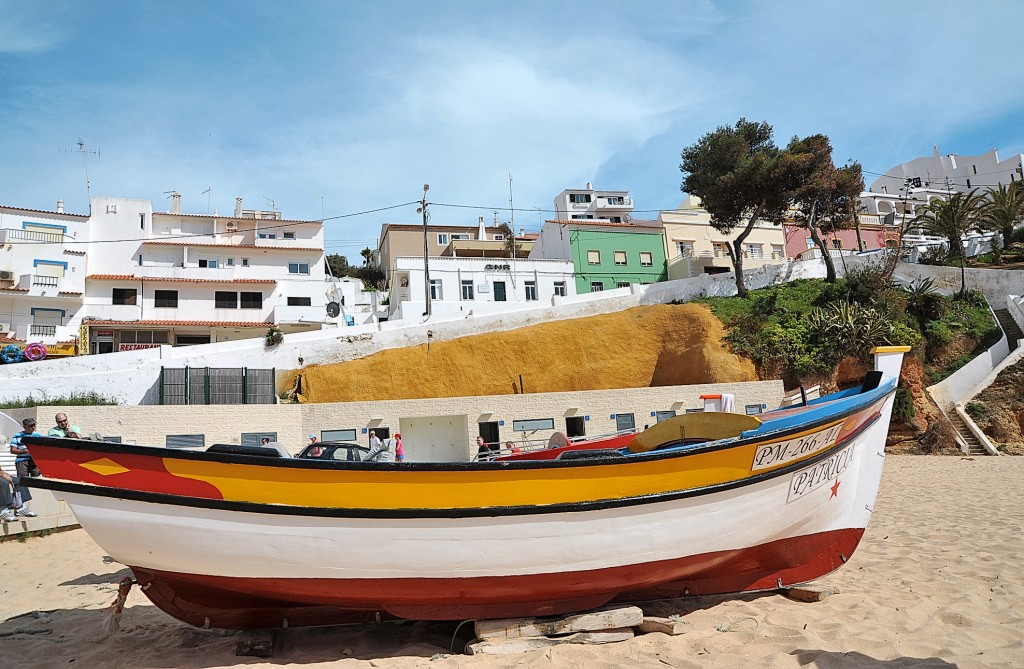 Ein bunte Fischerboot liegt am Strand mit weißen Häusern im Hintergrund