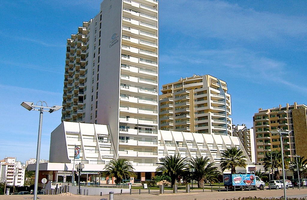 Moderne Hotelgebäude mit Palmen und Strandpromenade im Sonnenschein.